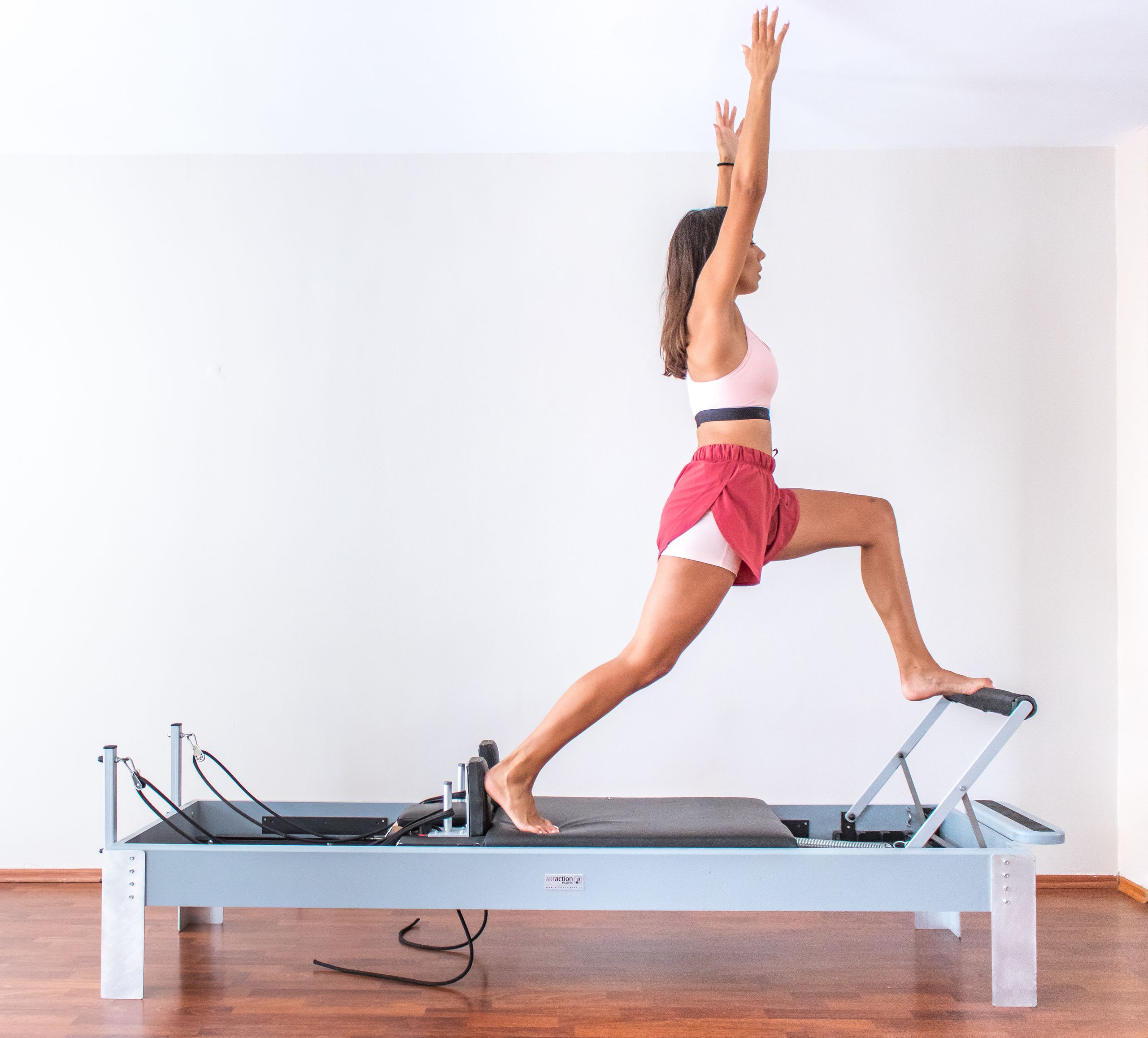 A woman exercises on a pilates reformer indoors, showcasing balance and fitness. Side view.