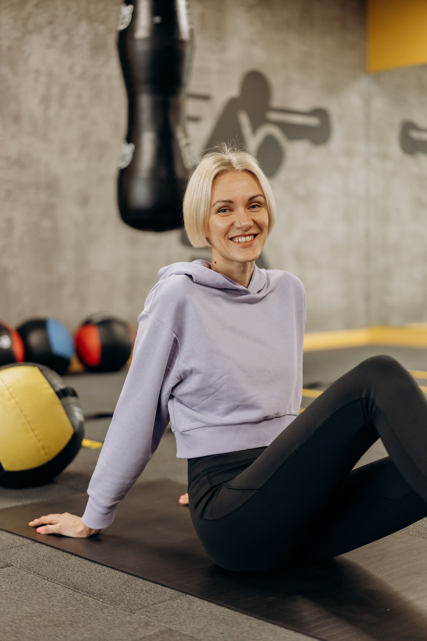 Fit and healthy woman smiling while stretching on a gym mat with exercise equipment around.
